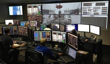 一个控制室，工人们在他们的工作站，一个显示实时画面和数据的视频墙