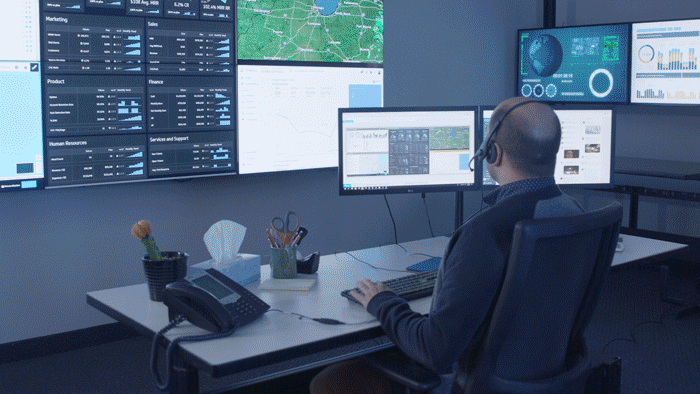 GIF of logistics employee typing at his office desk in front of a video wall, then remotely from his home desk in front of a window