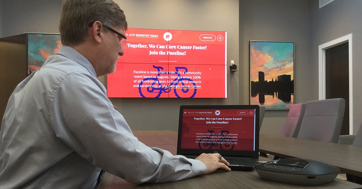 佐治亚州医学院的会议室，一名男子使用他的笔记本电脑和Userful将一个网页显示在他身后的视频墙上