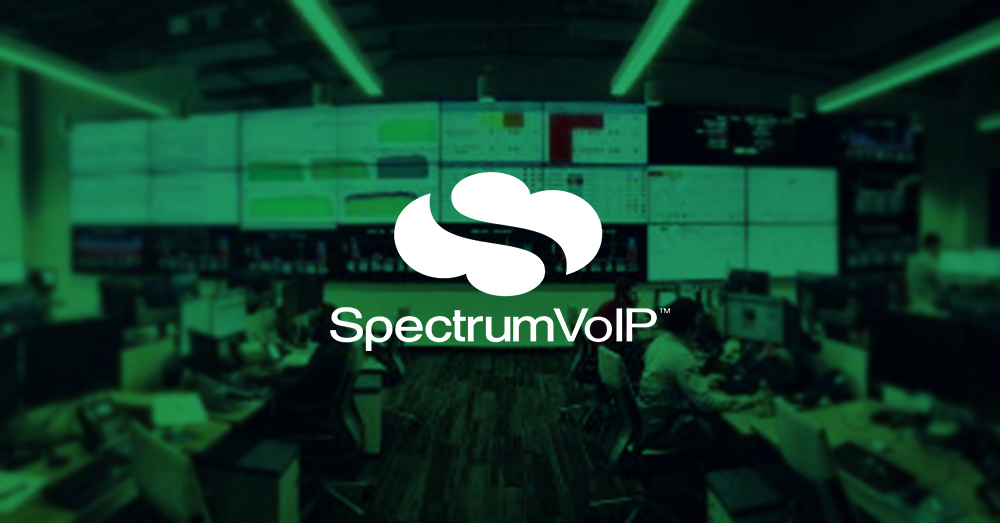 空旷的SpectrumVoIP网络运营中心，有许多工作站和一个较大的视频墙，显示带有绿色覆盖层和标志的数据仪表板