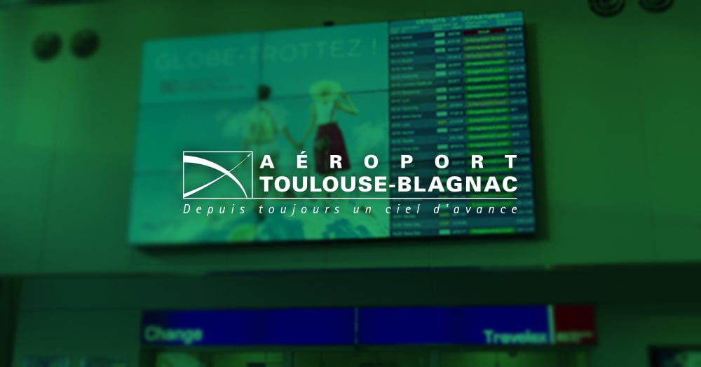 图卢兹-布拉格纳克机场的视频墙，显示广告和航班起飞时间，上面有绿色的覆盖物和标志。