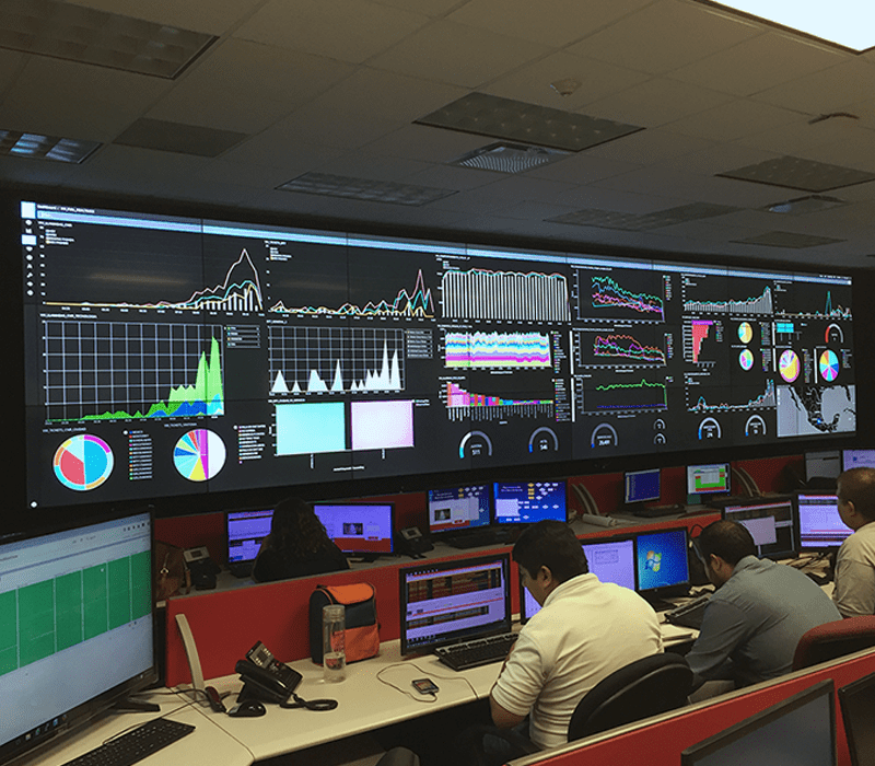 在控制室工作的员工，在带有显示数据仪表板的视频墙的工作站上工作。