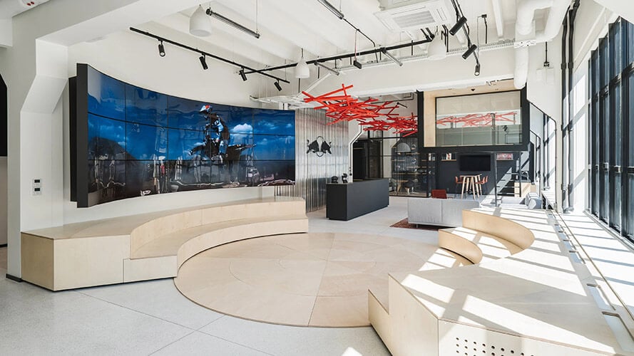 Redbull Poland Headquarters Lobby, with staircase shapped sitting area, reception desk, and a curved video wall displaying a Red Bull Commercial