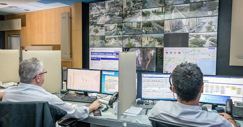 两名EMT员工通过他们的工作站和显示实时摄像画面、交通地图和网站的视频墙来监控交通运行情况。