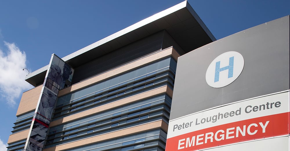 A photo of the Peter Lougheed Center Hospital emergency sign, and hospital building against a blue sky