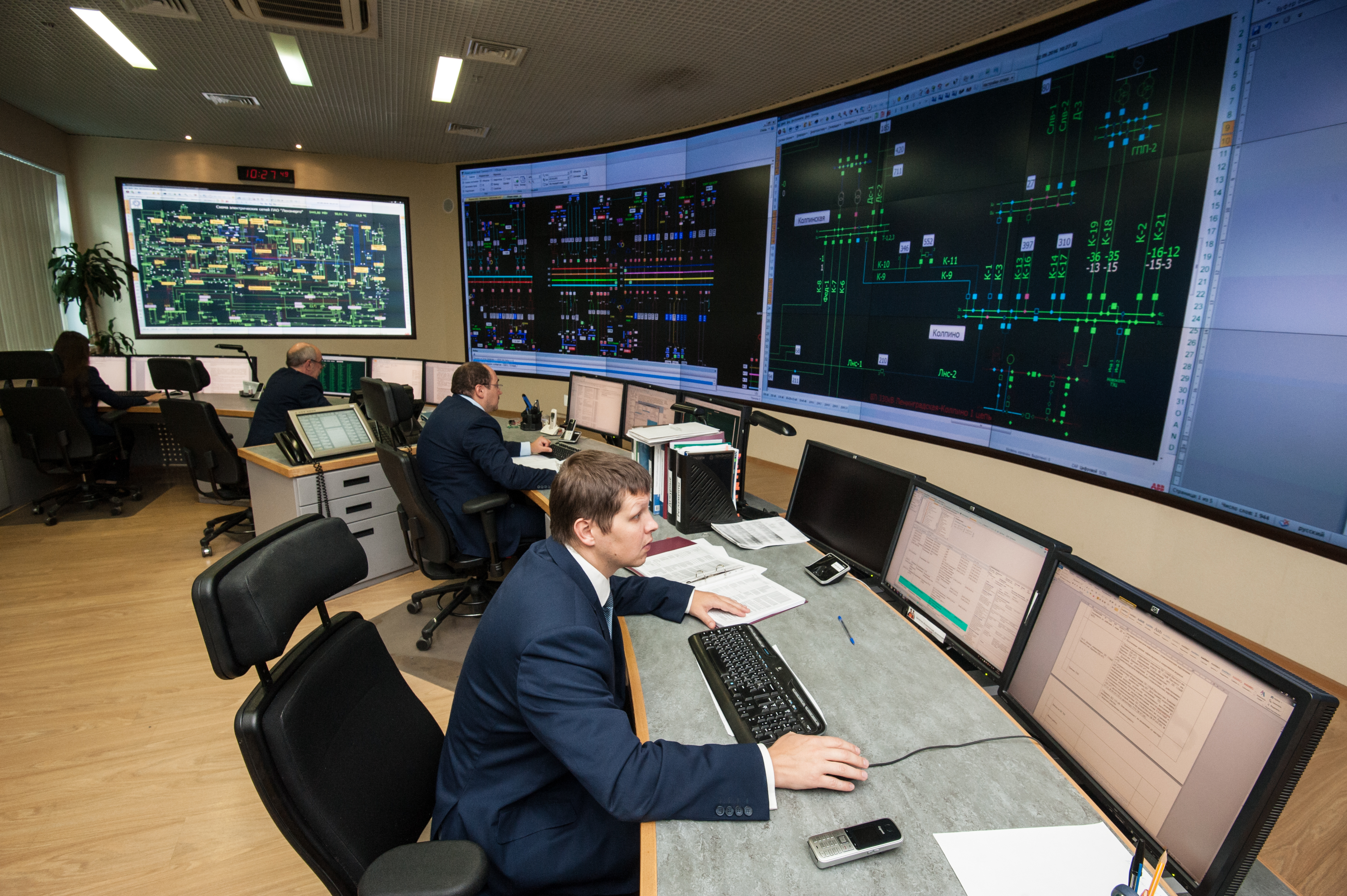 Employees working in a control room at workstations with video walls displaying IT infrastructure data