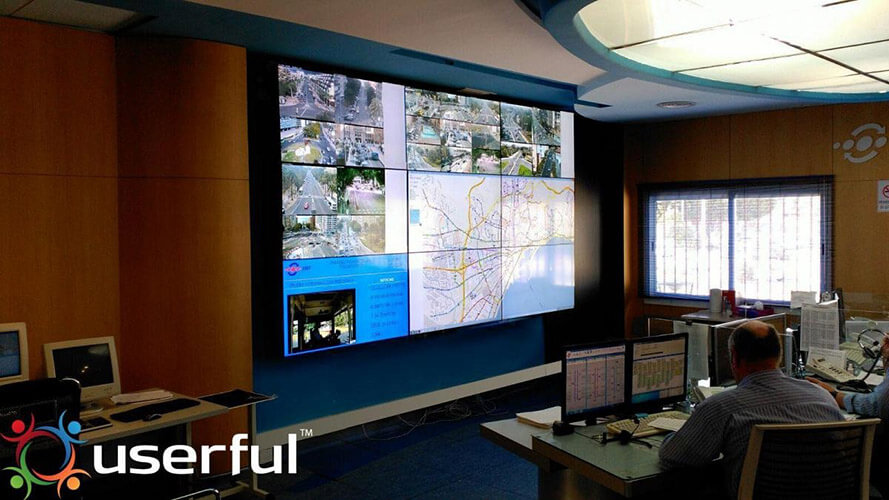 两名EMT员工通过他们的工作站和显示实时摄像画面、交通地图和网站的视频墙来监控交通运行情况。